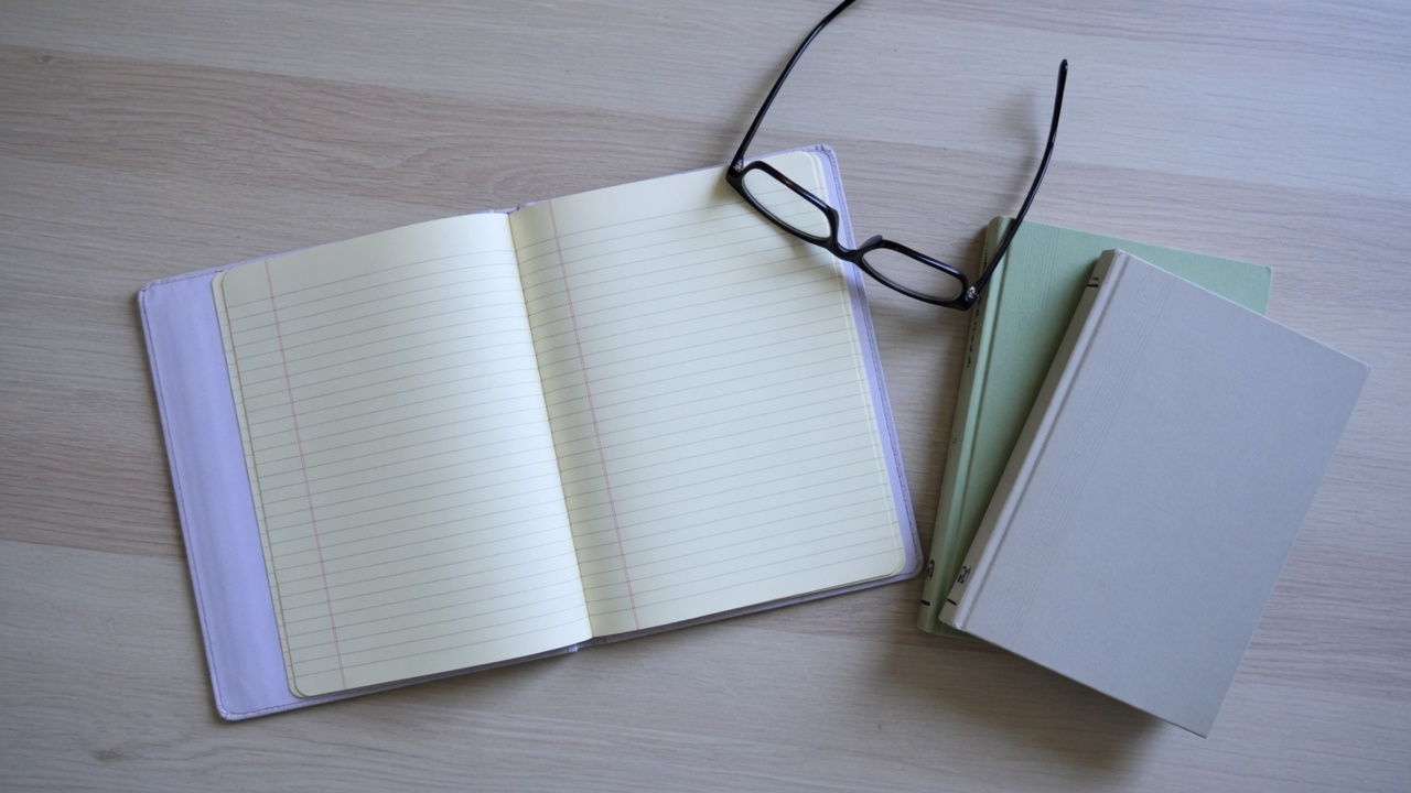 An open notebook and two books on a desk.